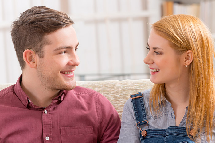 Young man with hearing aid smiling with a young woman